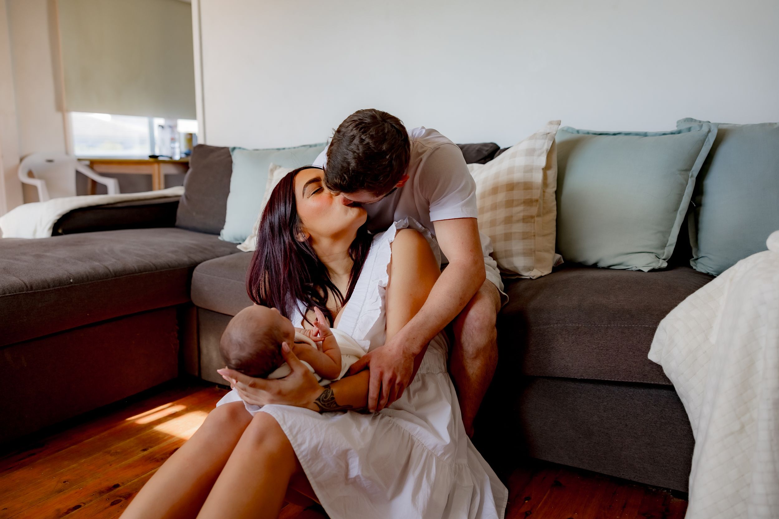 Intimate moment shared between couple with newborn on gray couch.