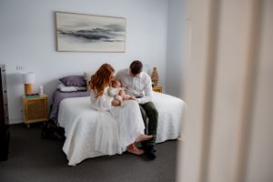 A couple sits on a white bed beneath a minimalist landscape painting.