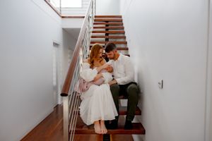 A couple shares an intimate moment on wooden stairs in a bright hallway.