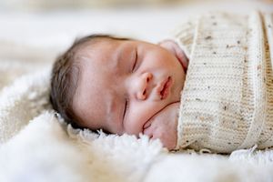 Peaceful newborn baby swaddled in a cream knit blanket, sleeping on a soft white fluffy surface.
