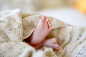 Tiny newborn baby feet peeking out from a soft cream knitted blanket, close-up infant photography.