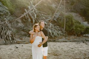 A couple embraces on a scenic beach with dramatic cliffs and golden sunlight.