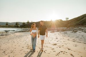 Couple walking hand in hand on beach at sunset with mountains in background.