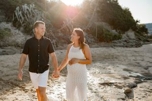 A couple walks hand in hand on a beach during sunset with cliffs in the background.