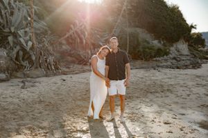 A couple stands together on a rocky beach during golden hour sunset.