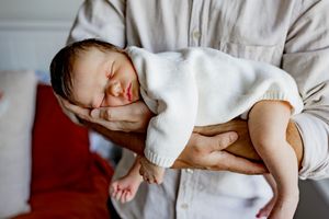 A sleeping baby rests peacefully in a cozy white sweater on soft bedding.