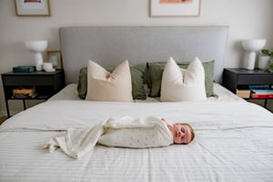 A sleeping newborn baby lies peacefully on a gray and white bed with decorative pillows.