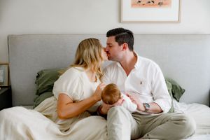 A tender family moment on a bed with a small infant in a bright modern bedroom.