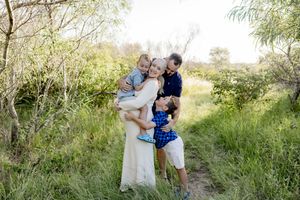 Family of four embracing outdoors in lush green meadow, parents holding children, natural light photography.