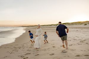 Family walking on a sandy beach at sunset, parents and two young children enjoying a peaceful coastal stroll.