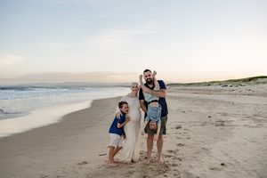 Happy family of four poses playfully on a sandy beach at sunset.