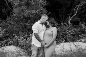 Black and white maternity photo of couple embracing in a natural outdoor setting.