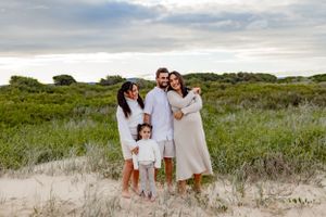 Family of four poses together on sandy dunes with green vegetation in background.