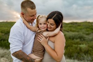 Family of three share a loving embrace outdoors during golden hour.