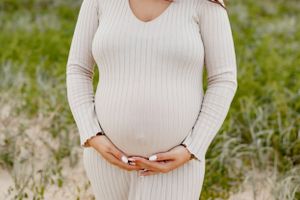 Close up of pregnant belly with hands gently cradling bump in ribbed white dress.