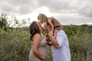 A tender family moment captured outdoors with a small child being lifted up against a natural background.