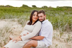 Intimate maternity photo of couple sitting together on coastal dunes.