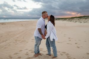 Couple sharing intimate moment on beach with cloudy sunset sky.