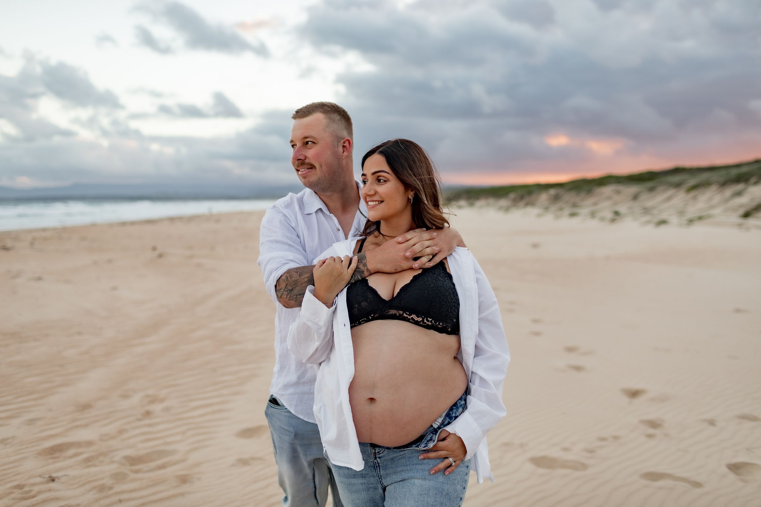 Maternity photo of couple on beach during sunset wearing casual attire.