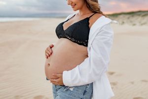 Close-up maternity photo showing pregnant belly on beach at sunset.