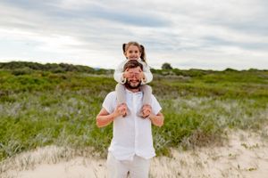 Playful outdoor moment between parent and child in white clothing against natural scenery.