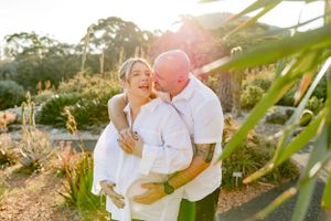 Couple embraces during golden hour with sunlight filtering through tropical foliage.