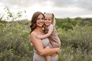 Mother and child share an embrace while posing for a portrait in a natural outdoor setting.