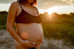 Silhouetted maternity portrait during golden hour showing pregnant belly in natural setting.