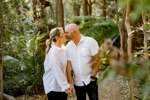 Romantic couple in white shirts share an intimate moment among lush greenery and trees.
