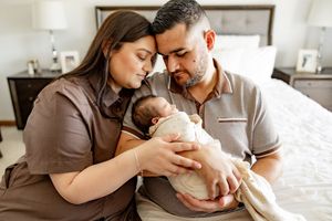 A tender family moment captured in warm tones as parents lovingly cradle their newborn baby in a bright home setting.