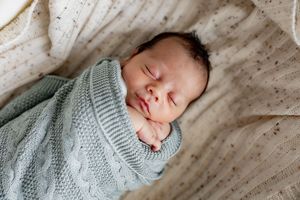 Sleeping newborn wrapped in soft mint green knit blanket against white textured background.