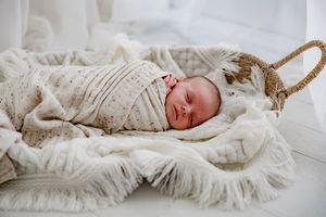 Peaceful newborn baby sleeping while swaddled in cream colored textured blankets on white backdrop.