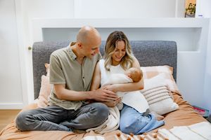 Couple relaxing together on white couch while looking at documents and using laptop computer.