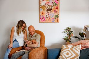 A series of five connected photos showing tender moments on an orange armchair with floral artwork in the background.