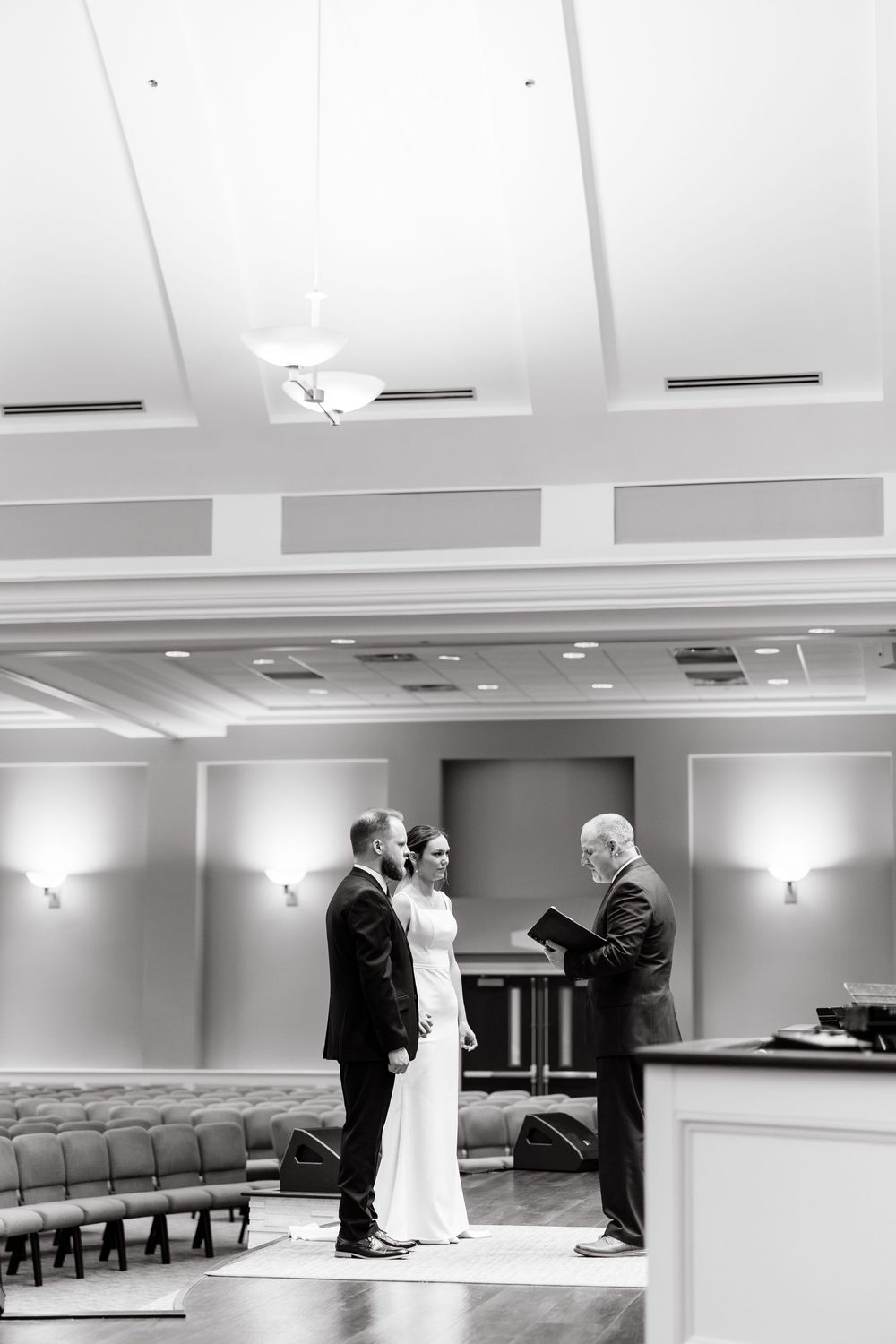 Black and white panoramic sequence showing a wedding ceremony taking place in a simple church hall with rows of seating.