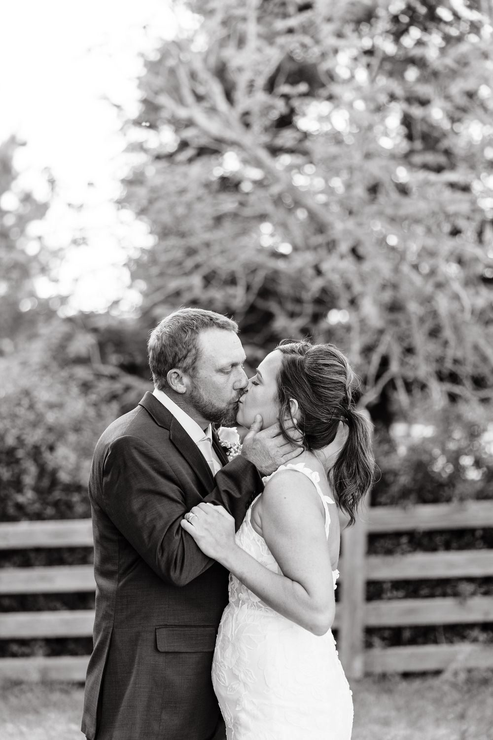 A romantic black and white wedding photo sequence shows a couple sharing a tender kiss outdoors by a wooden fence.