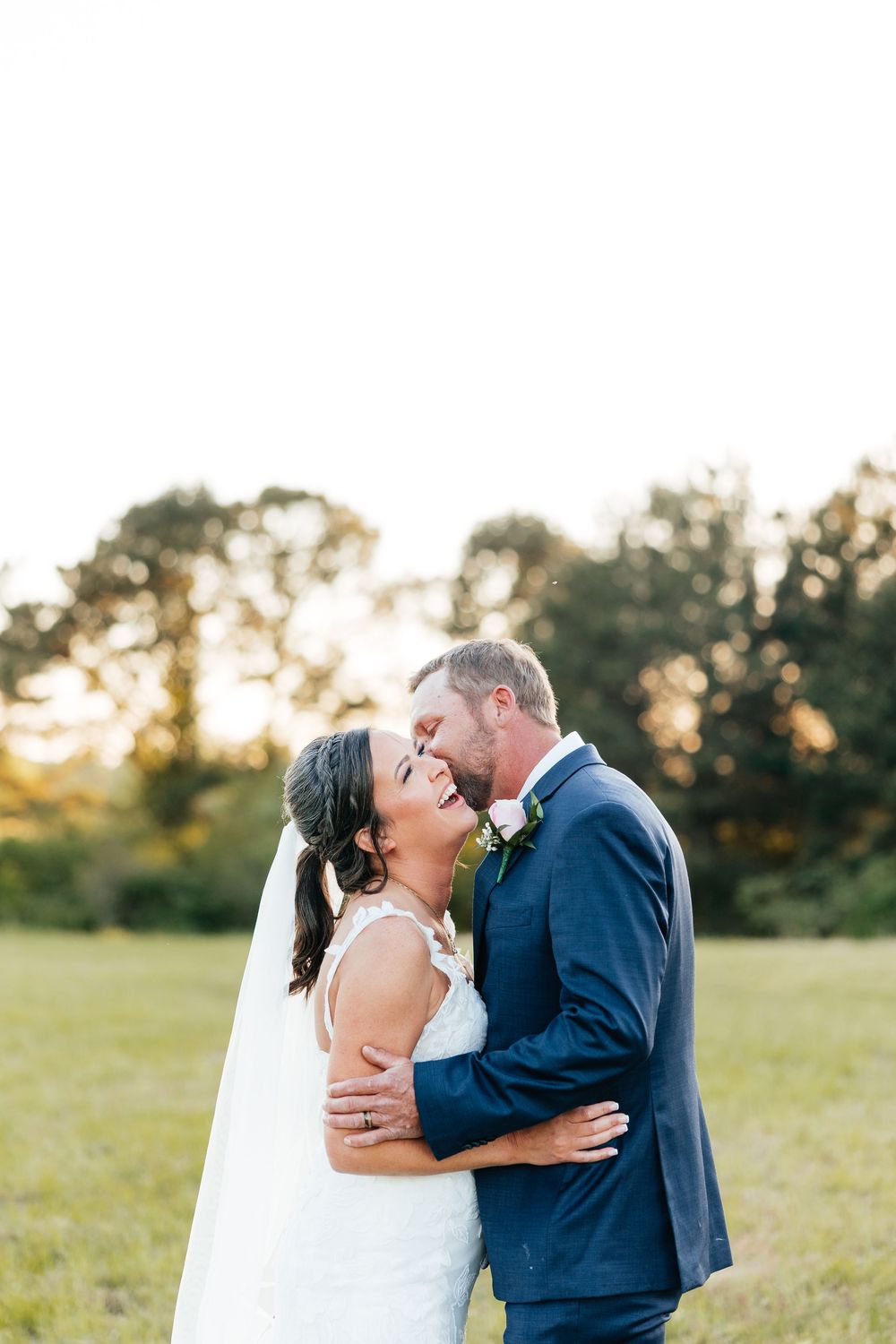 A romantic wedding couple shares intimate moments in a sunlit field at golden hour.