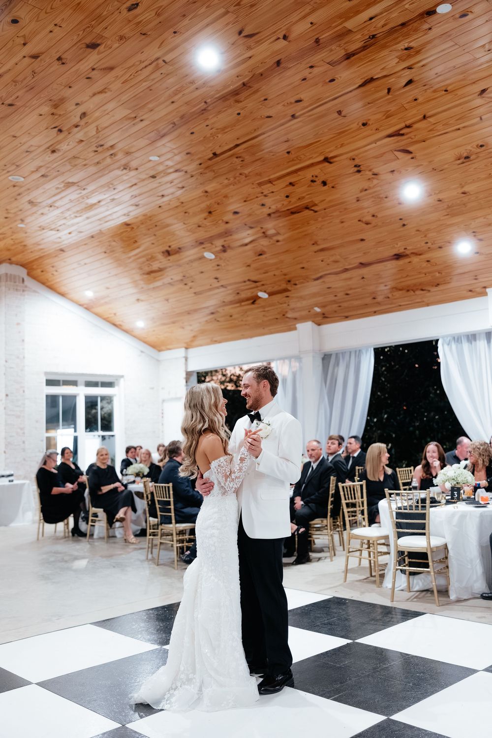 Bride and groom share first dance on black and white checkered floor in elegant wedding reception venue.