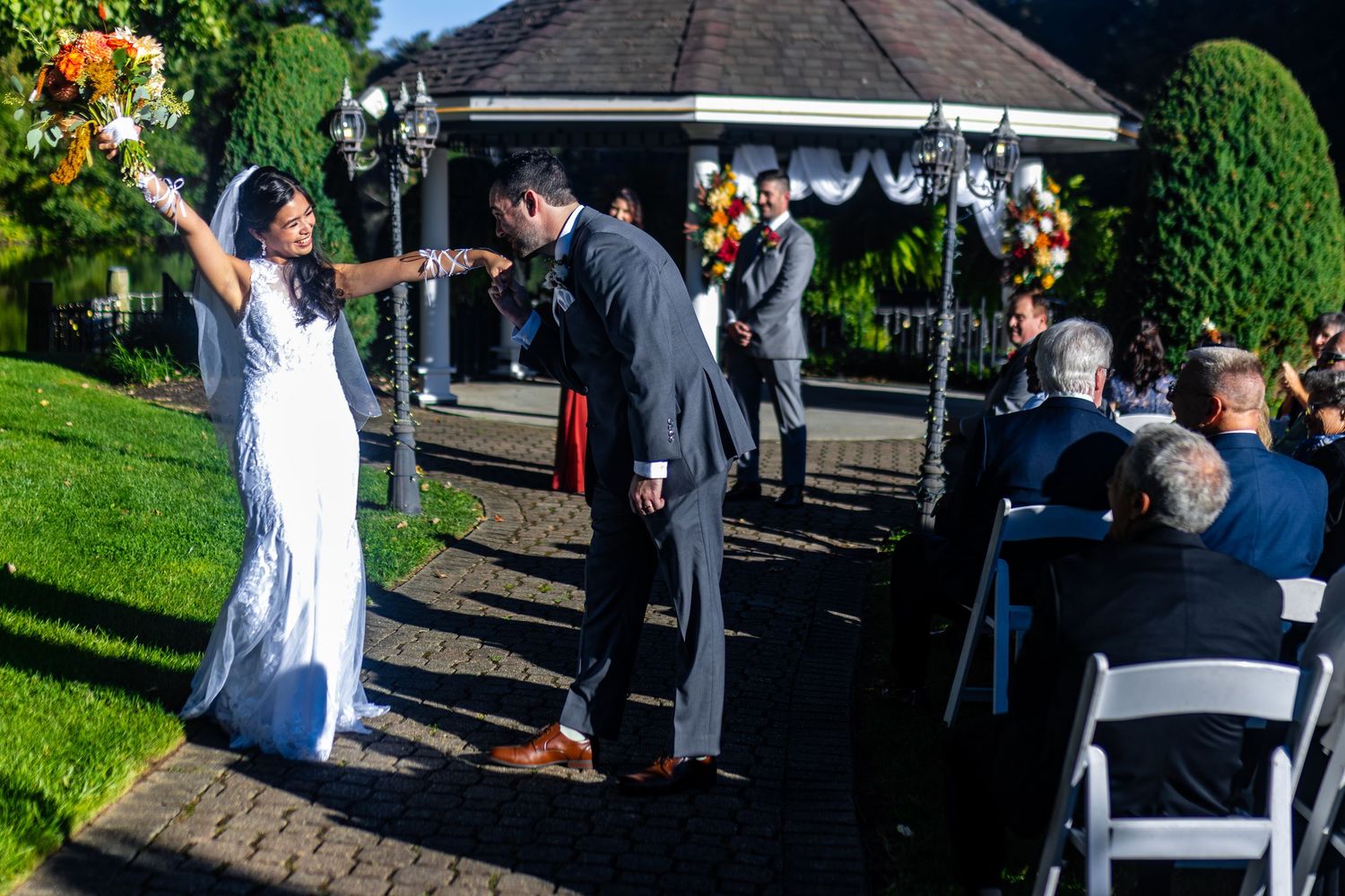 Wedding celebration at a decorated gazebo with guests seated on white chairs during an outdoor ceremony.