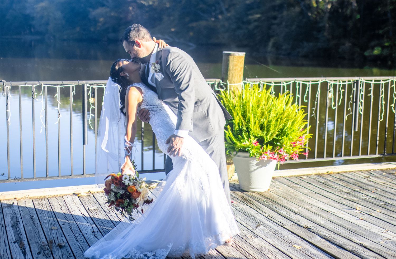 Couple in wedding attire sharing a romantic moment on a lakeside dock.