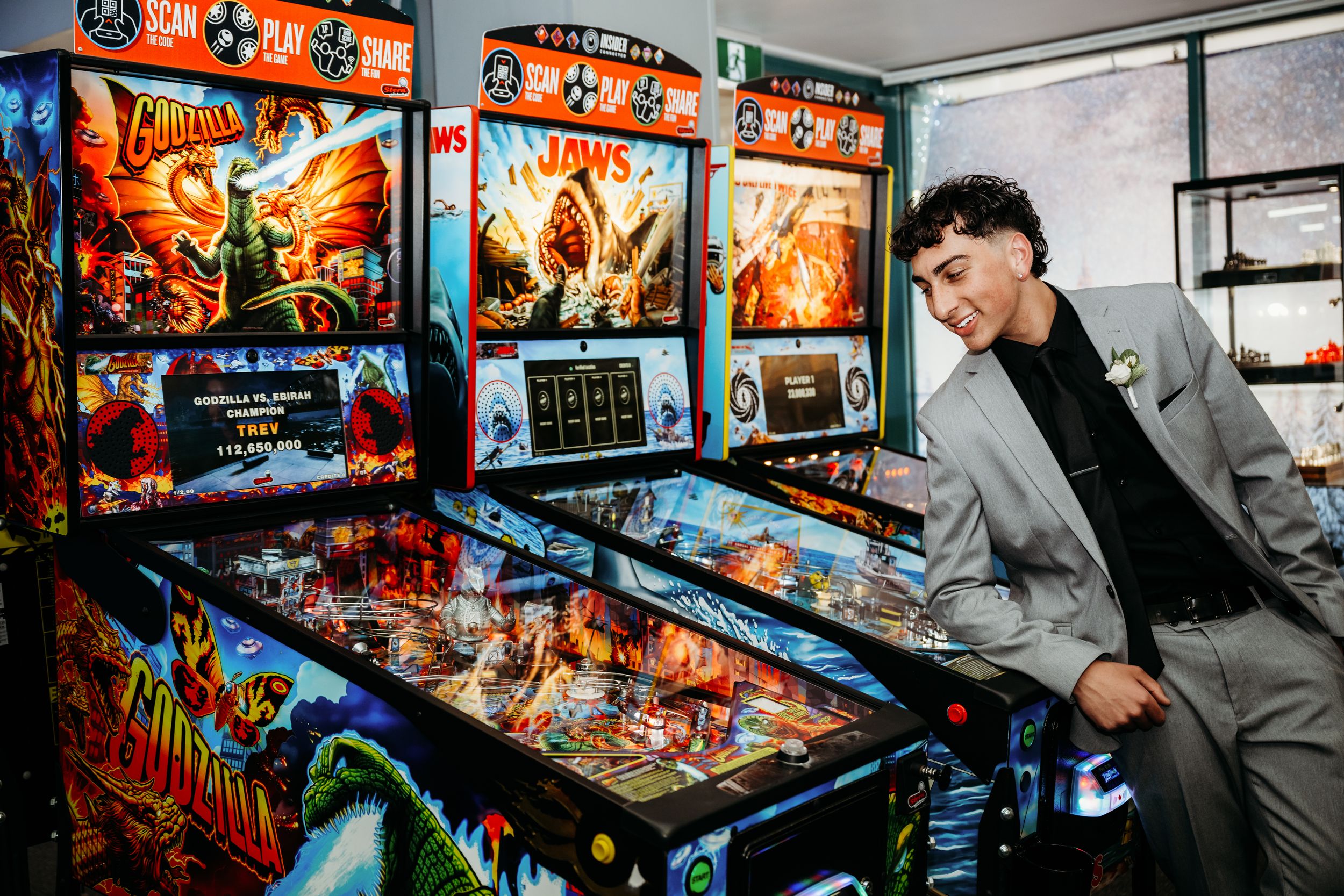 Colorful vintage pinball machines illuminate an arcade room as someone in gray attire enjoys playing the games.