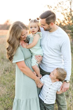 Mother and father cuddling their two young children together in a sunlit grassy field during a natural outdoor family portrait.