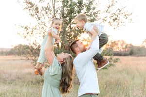 Parents lifting their young children into the air while playing together in a grassy field during a sunset family photo session.