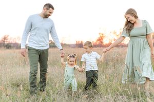 Family of four walking hand in hand through a grassy field during a golden-hour outdoor family photography session.