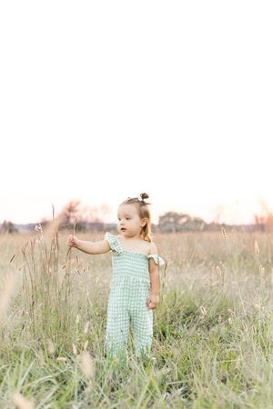 Young child wearing a light green outfit standing in a grassy wildflower field during a natural outdoor children's portrait session.