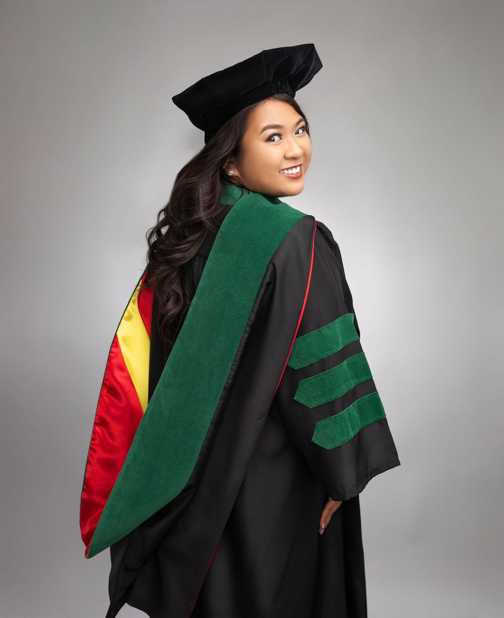 Graduate in academic regalia with green accents poses against gray backdrop.
