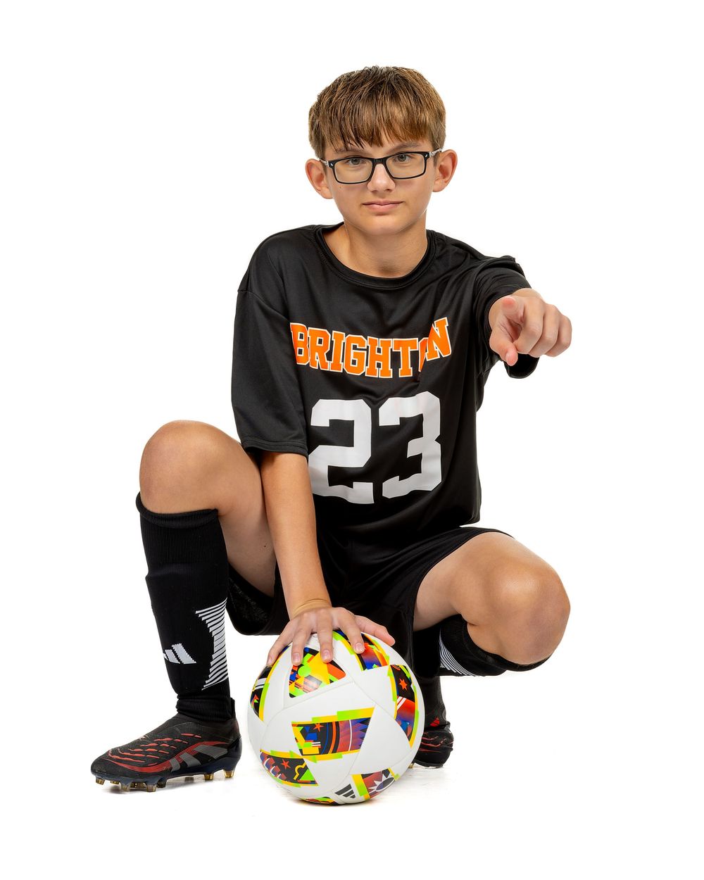 Young soccer player in black uniform crouches with ball in dynamic sequence of action poses.