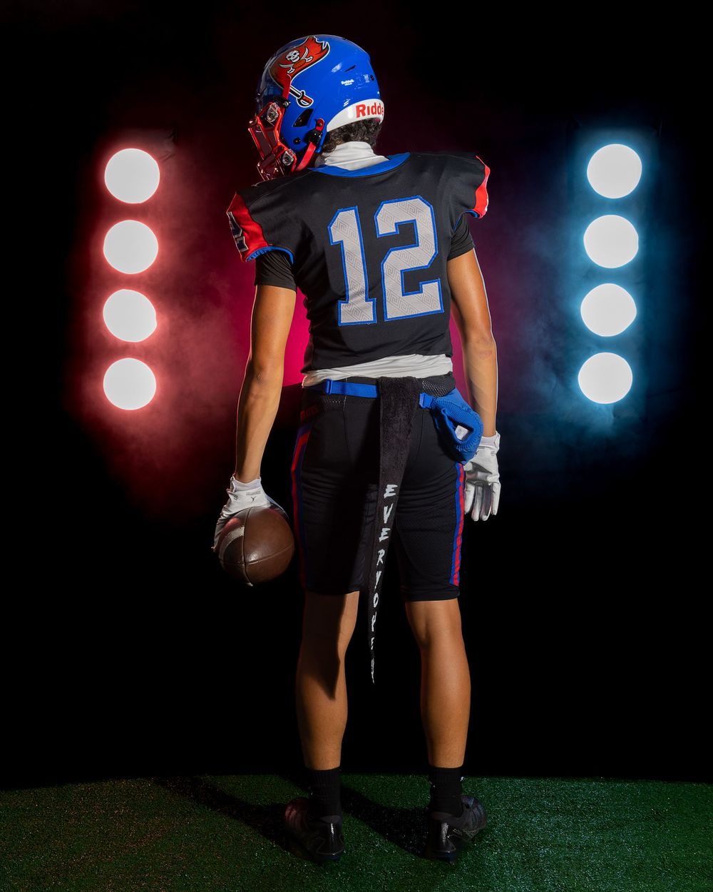 Football player in blue uniform holds ball against dramatic lighting backdrop.