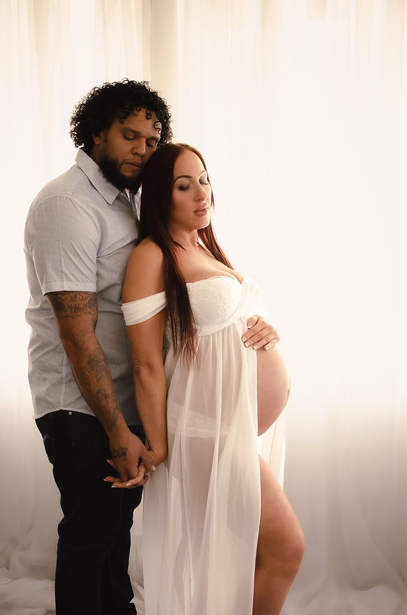 Romantic indoor maternity portrait of couple holding hands in soft light, captured by Denver maternity photographer.