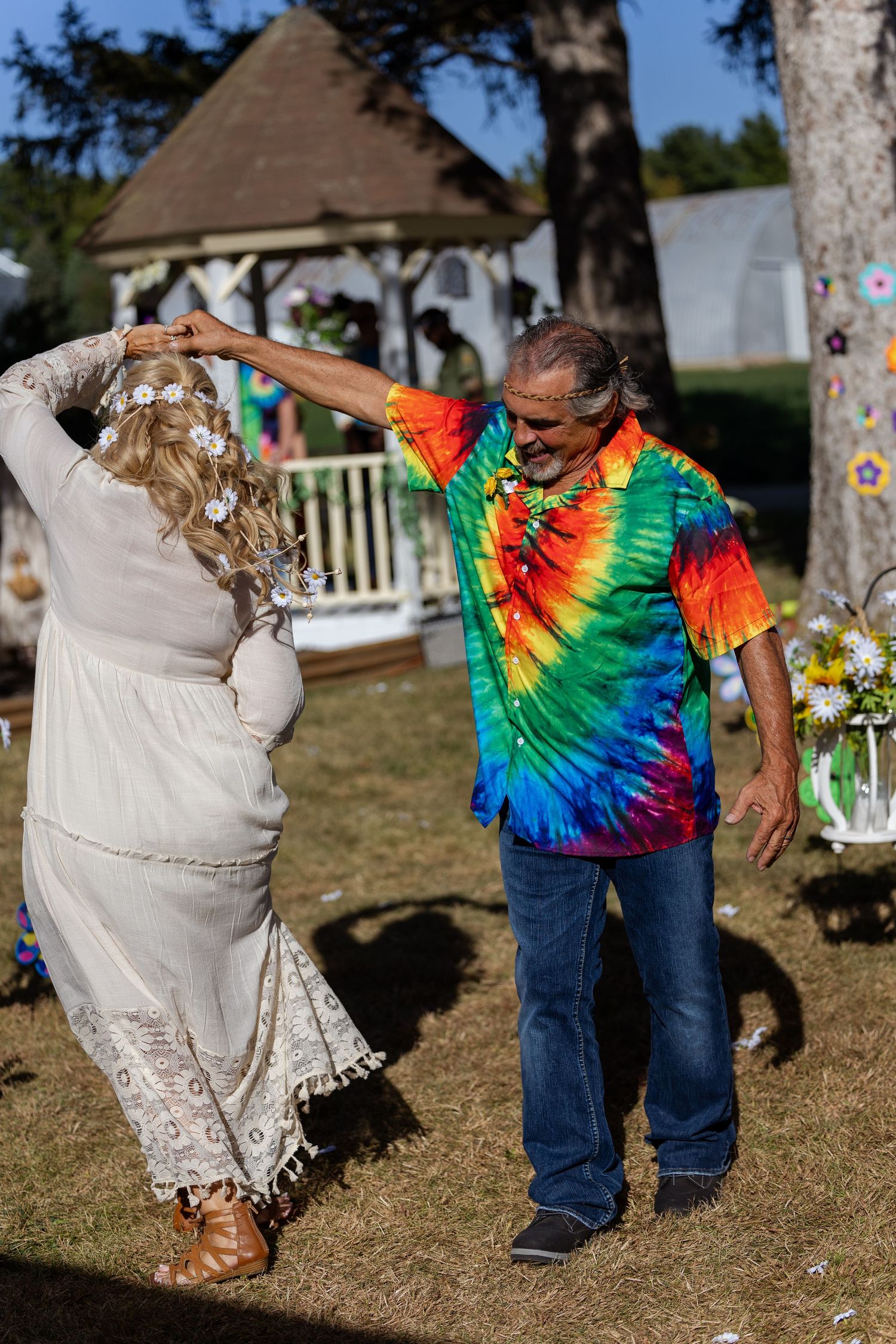 A dancing couple enjoys a moment outdoors, one wearing vibrant tie-dye and the other in a lace dress.